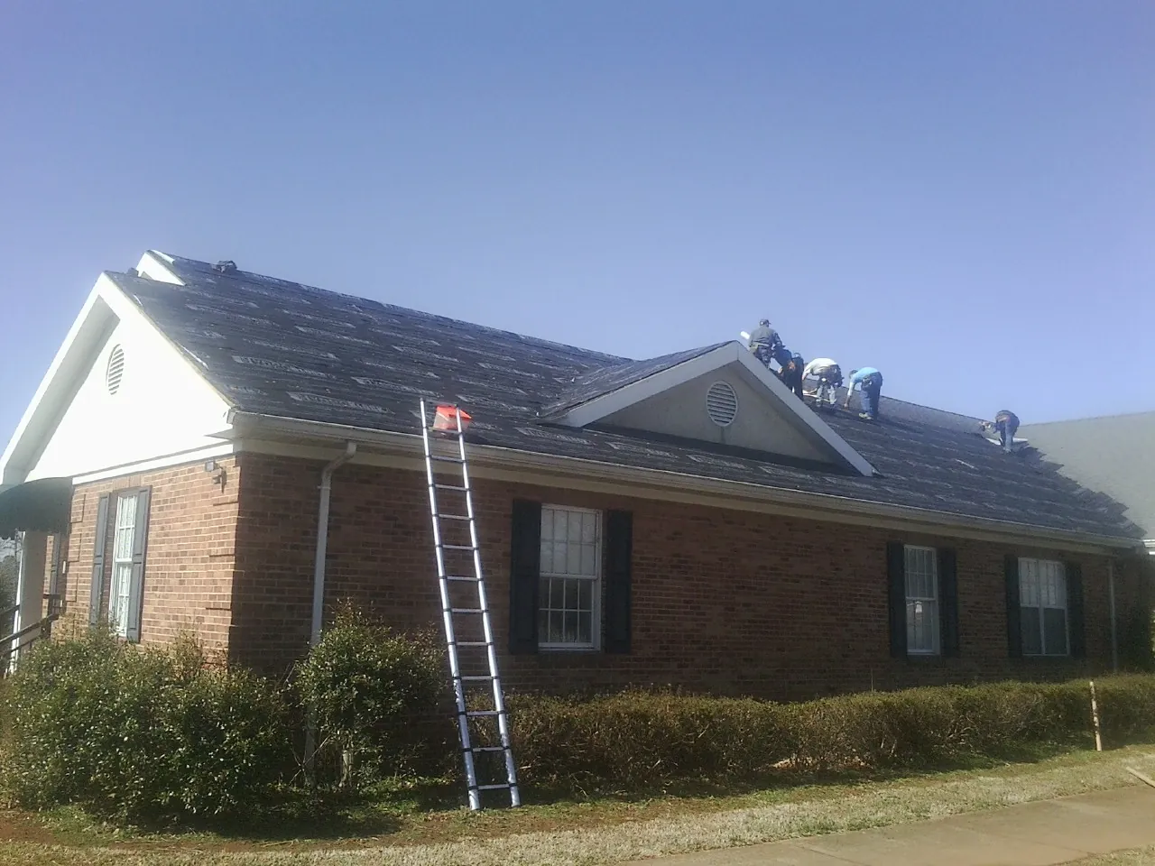 Crew tearing shingles off a brick ranch roof with a ladder set — Emergency Roof Repair work by our crew in Tujunga