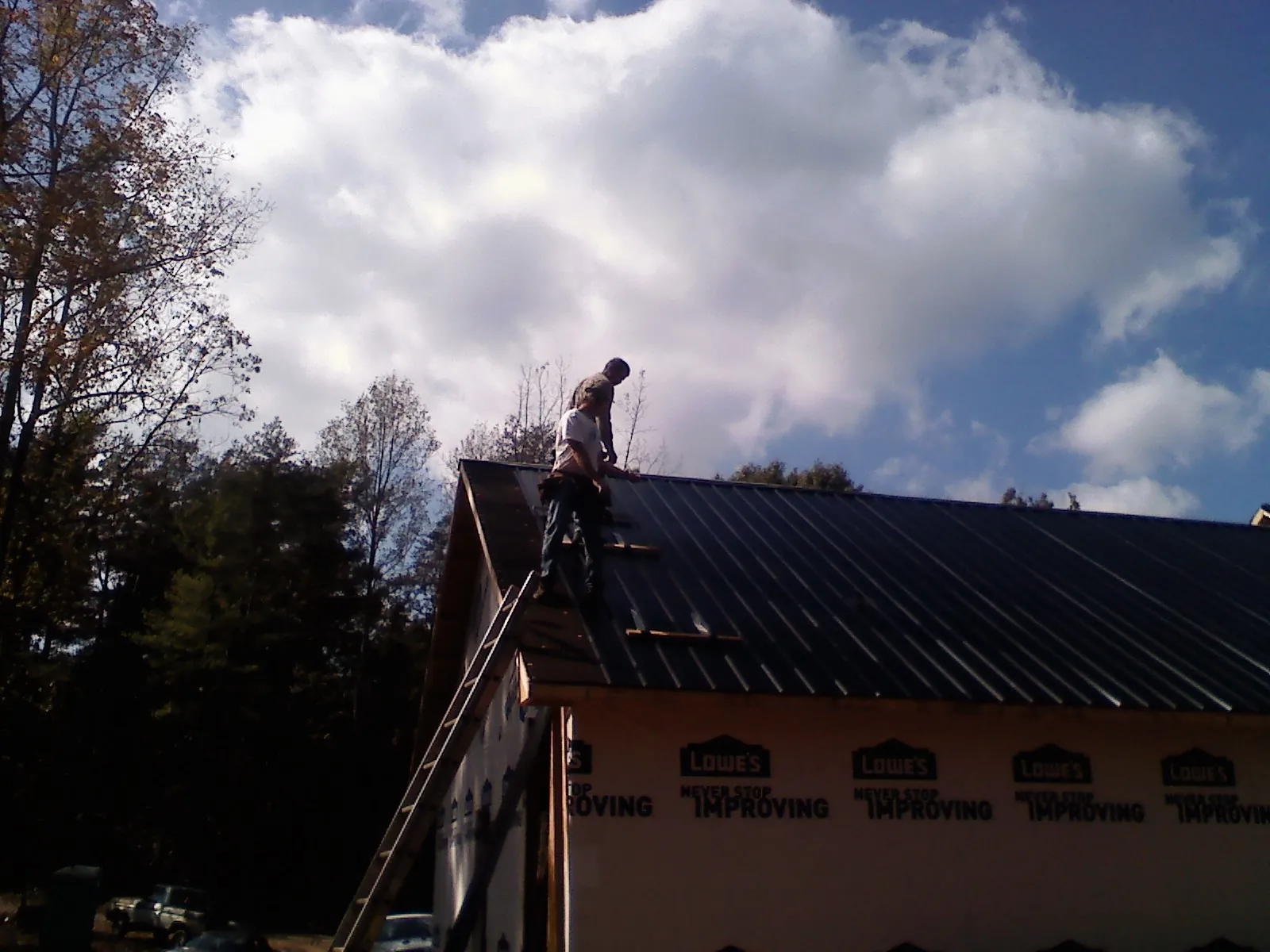 Roofer fastening dark metal panels high against a cloudy sky, from a Roof Inspection job in Tujunga