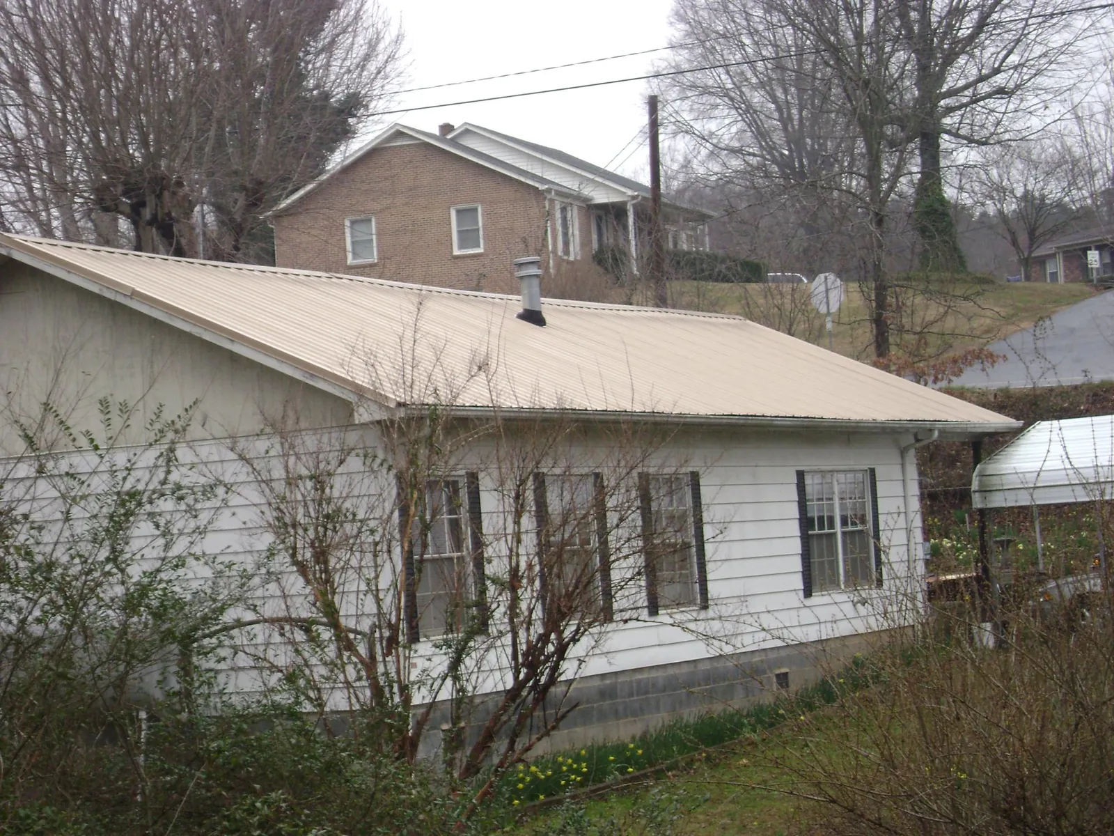 Tan metal roof on a white sided house set into a hillside — Commercial Roofing by Roofing Brothers in Tujunga
